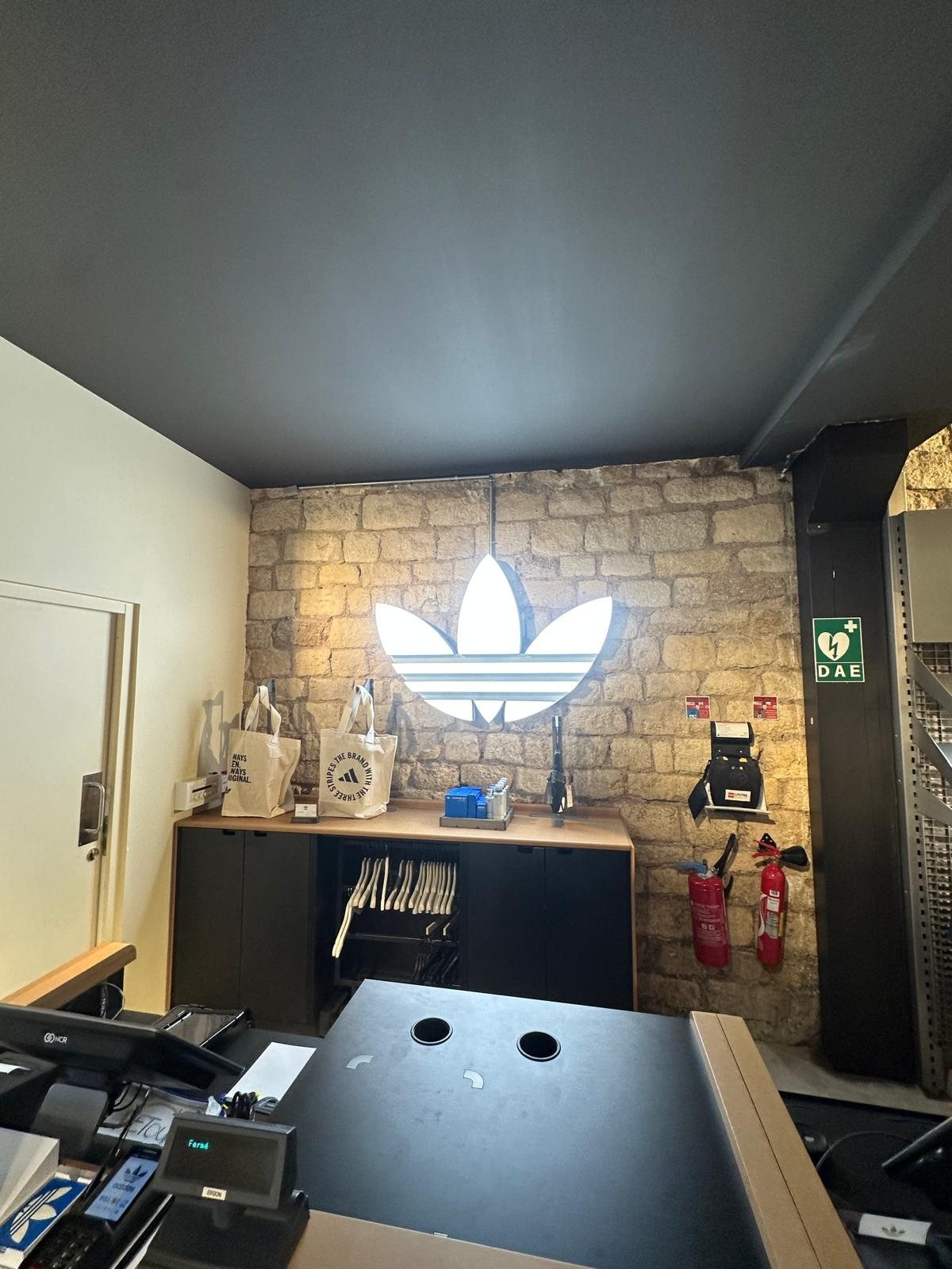 Logo lumineux Adidas installé sur un mur intérieur en pierre