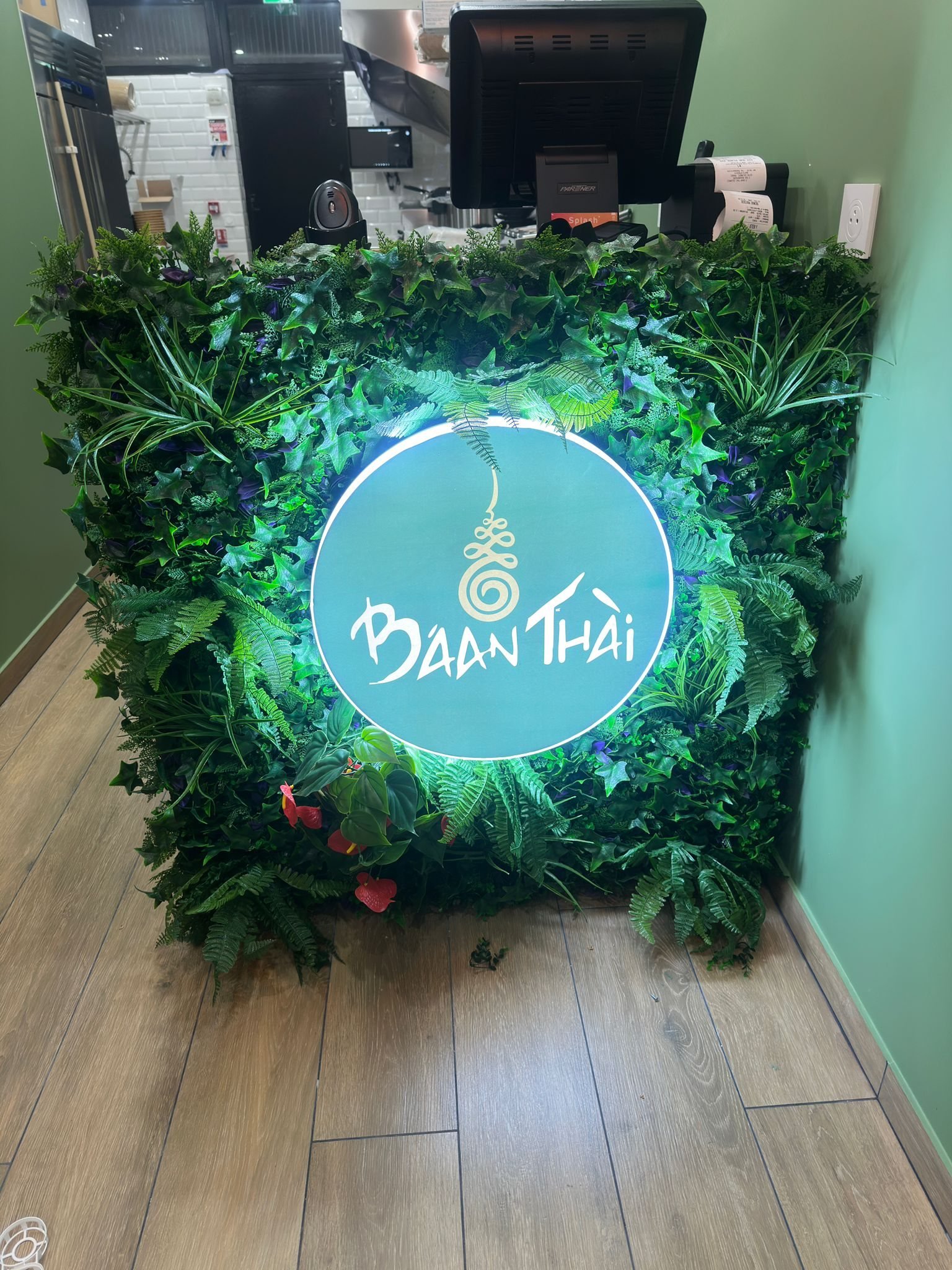 Logo lumineux intégré sur décor végétal derrière un comptoir